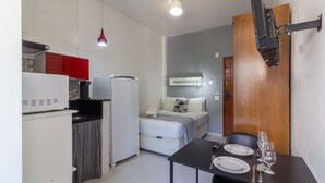 A compact room with a kitchenette, a bed, a dining table with chairs, and a mounted TV. - Moderno Studio en Rio de Janeiro T915 (Rio de Janeiro)