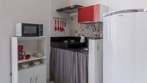 A compact kitchen with a microwave, refrigerator, and a hanging red pendant light. - Moderno Studio en Rio de Janeiro T915 (Rio de Janeiro)