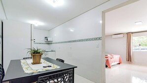 Una habitación limpia y moderna con una mesa de comedor, sillas, una planta en maceta y una cama con una manta rosa.