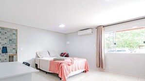 Un dormitorio con cama, mesita de noche, ventana con cortinas y aire acondicionado instalado en la pared.