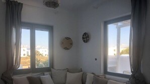 Un canapé d’angle avec des coussins, deux fenêtres avec des rideaux et des éléments de décoration murale.