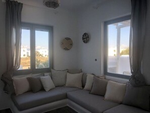 A corner sofa with cushions, two windows with curtains, and wall decorations. - Casa Magnifica, Mikri Vigla Naxos (Mikri Vigla)