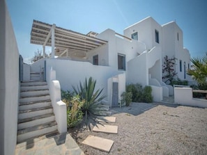 A modern white building with a staircase leading to a covered area, surrounded by gravel and sparse vegetation. - Casa Magnifica, Mikri Vigla Naxos (Mikri Vigla)