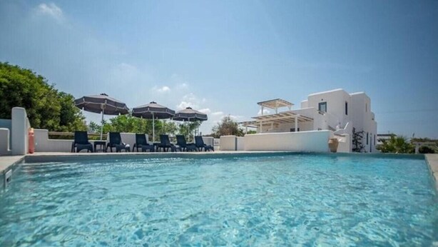Une piscine à l’eau claire, des chaises longues, des parasols et un bâtiment blanc en arrière-plan.