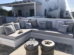 A modern outdoor seating area with a sectional sofa, two round tables, and a pergola structure. - Casa Magnifica, Mikri Vigla Naxos (Mikri Vigla)