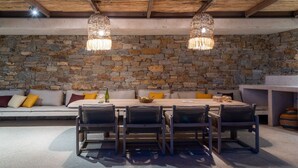 Une pièce aux murs de pierre, avec un plafond en bois, un banc en pierre et une table entourée de chaises.