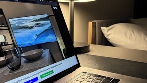 Ein Laptop auf einem Tisch, mit einem Facebook-Anmeldebildschirm, einer Lampe und einem Bett im Hintergrund.