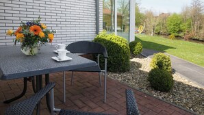 Een terras buiten met een tafel, stoelen en een bloevas.
