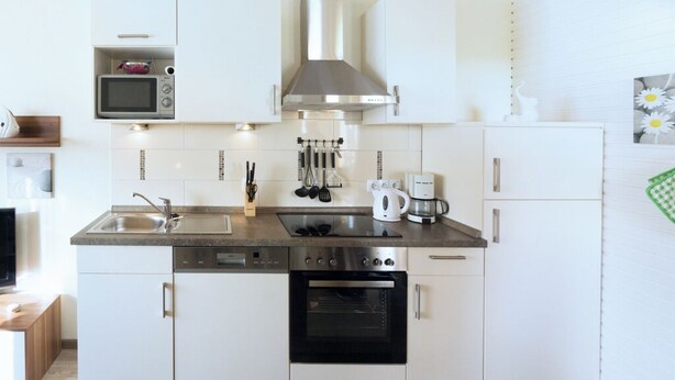 Een moderne keuken met witte kastjes, een magnetron, een fornuis, een oven en een koffiezetapparaat.