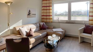 Een woonkamer met een bank, fauteuil, glazen salontafel en een radiator.