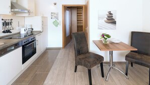 Een moderne keuken met een fornuis, oven en koffiezetapparaat. Er is een eethoek met een tafel en twee stoelen.