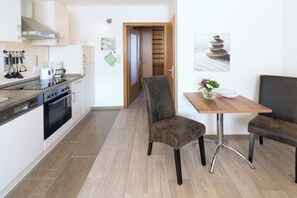 A modern kitchen with a stove, oven, and coffee maker. There is a dining area with a table and two chairs. - House Nordseekrabbe apartment 9, Carolinenhof 7, 300m to harbor terrace garden (Neuharlingersiel)