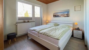 Een slaapkamer met een bed, nachtkastjes, een raam, een radiator en een schilderij aan de muur.