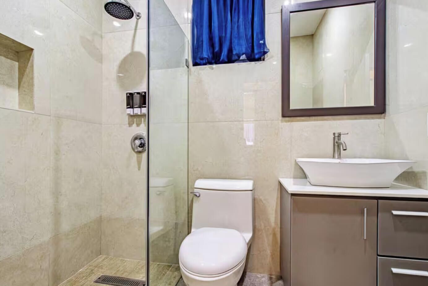 Un bagno con doccia vetrata, un WC bianco, un lavandino con specchio sopra e una tenda blu.