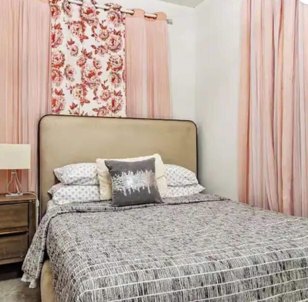 A bedroom with a bed, a nightstand, a lamp, and curtains.
