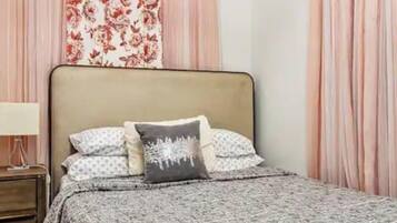 A bedroom with a bed, a nightstand, a lamp, and curtains.