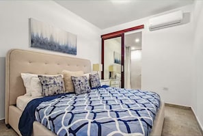 A bedroom with a bed, a nightstand, a lamp, a painting, and a door.