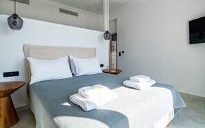 Ein modernes Hotelzimmer mit einem großen Bett, zwei Kissen, einem Nachttisch, einer Pendelleuchte und einem an der Wand befestigten Fernseher.