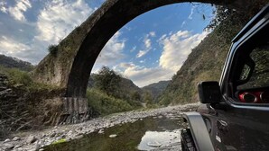 A vehicle passing under a stone bridge with a river and hills in the background. - Nahualli Hospedaje Boutique /5 recámaras céntrico (Zacatlán)
