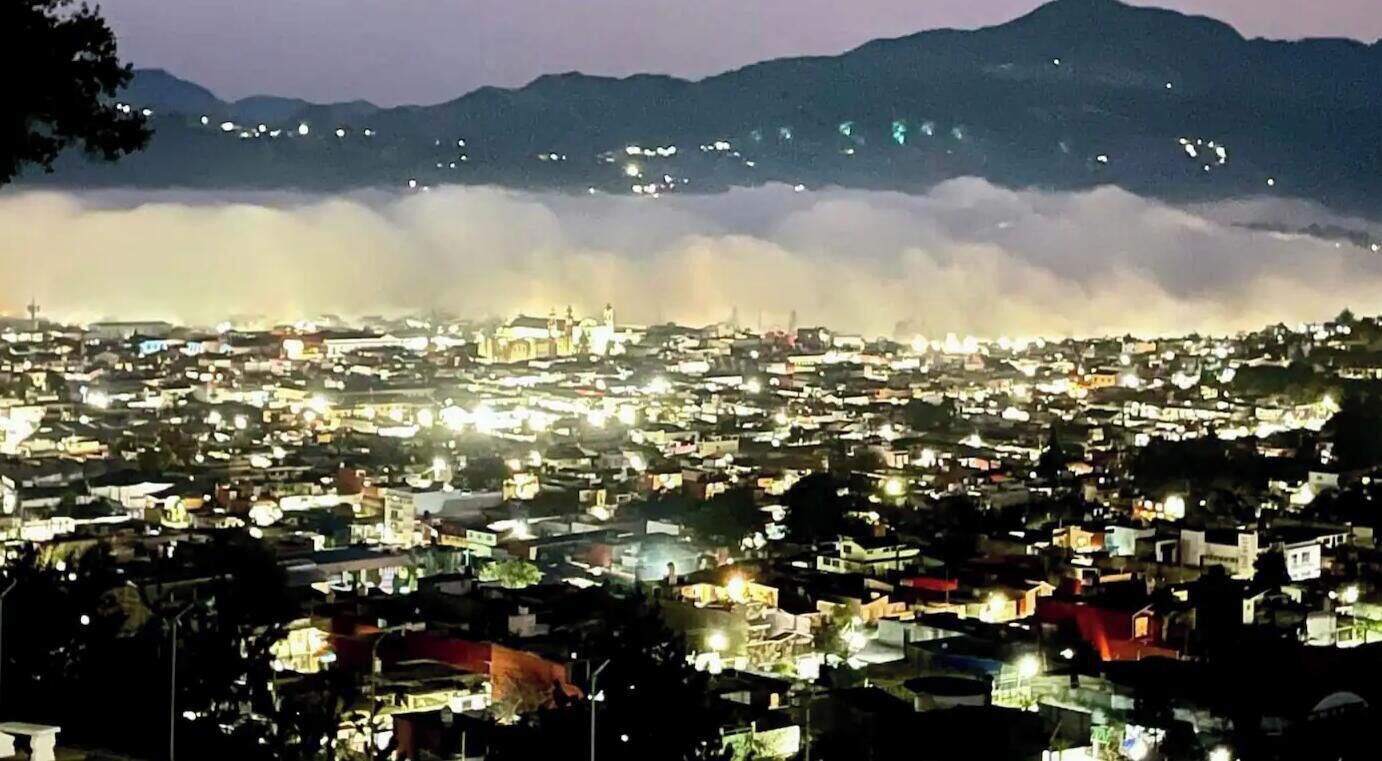 A cityscape at night with buildings and a mountain in the background.