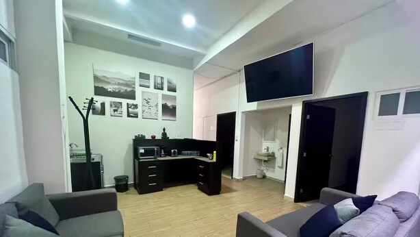 A modern living room with a sofa, a dining area with a kitchen counter, and a flat-screen TV mounted on the wall. - Nahualli Hospedaje Boutique /5 recámaras céntrico (Zacatlán)