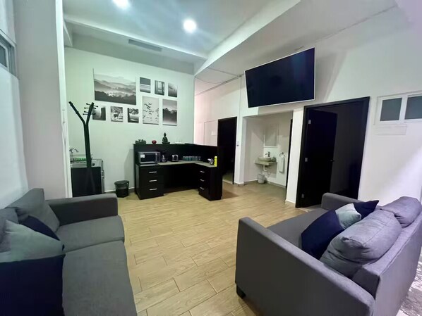 A modern living room with a sofa, a dining area with a kitchen counter, and a flat-screen TV mounted on the wall.