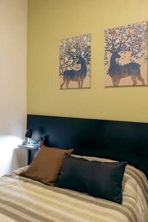 Un lit avec une literie à rayures, une tête de lit noire et deux tableaux représentant des cerfs, accrochés au mur.