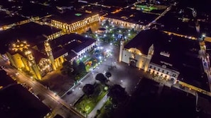 Vue aérienne d’une place historique illuminée la nuit, avec des bâtiments éclairés et une place centrale.