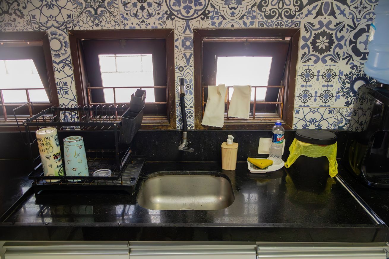 A kitchen with a sink, stove, and windows with curtains.