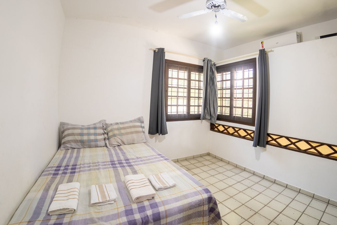 Um quarto com cama, janela com cortinas, ventilador de teto e piso de azulejos.