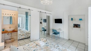 Habitación de hotel con una cama grande, baño con lavamanos y espejo, escritorio, silla y televisor.