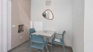 Una habitación pequeña con una mesa blanca y dos sillas, un espejo montado en la pared y un estante pequeño.