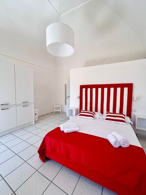 Une chambre d’hôtel moderne avec un grand lit, une armoire blanche, une petite table de chevet et un luminaire blanc au plafond.