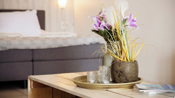 A bed with white bedding, a grey sofa, a wooden table with a vase of flowers, and a tray with two glasses. - Studio Bientu- centrally located-near trendy beaches (Sint Michiel)