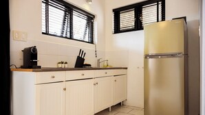 A kitchen with white cabinets, a stainless steel refrigerator, a coffee maker, and two windows with blinds. - Studio Bientu- centrally located-near trendy beaches (Sint Michiel)