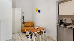 A compact kitchen with a wooden table, white chairs, a small refrigerator, and a sofa. - Apartment 'Yellow Room' with Sea View, Wi-Fi and Air Conditioning (Meta)