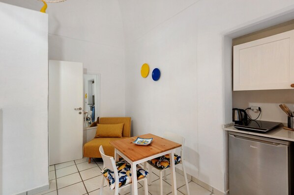 Una cocina compacta con una mesa de madera, sillas blancas, un refrigerador pequeño y un sofá.