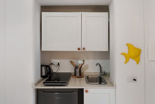 Een kleine keuken met witte kastjes, een koffiezetapparaat, een broodrooster, een spoelbak en een vaatwasser.