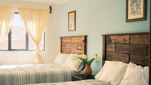 A hotel room with two beds, a window with curtains, a vase with flowers, and a framed picture on the wall. - Spacious Downtown Apartment / Family Friendly + Parking (Zacatlán)