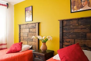 A room with two beds, a wooden headboard, a vase with flowers, and a painting on the wall.