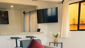 A modern living room with a grey sofa, a red pillow, a flat-screen TV, and a small table with a vase of flowers. - Spacious Downtown Apartment / Family Friendly + Parking (Zacatlán)