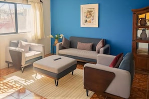 A living room with a sofa, armchair, ottoman, and a cabinet.