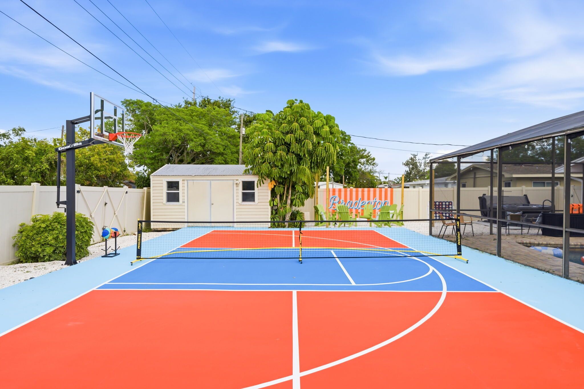 Un campo da basket all'aperto con canestro, un piccolo deposito e un albero sullo sfondo.