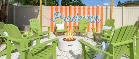 Eine Terrasse mit grünen Adirondack-Stühlen, einer Feuerstelle und einem Zaun, auf dem 'Bradepton' steht.