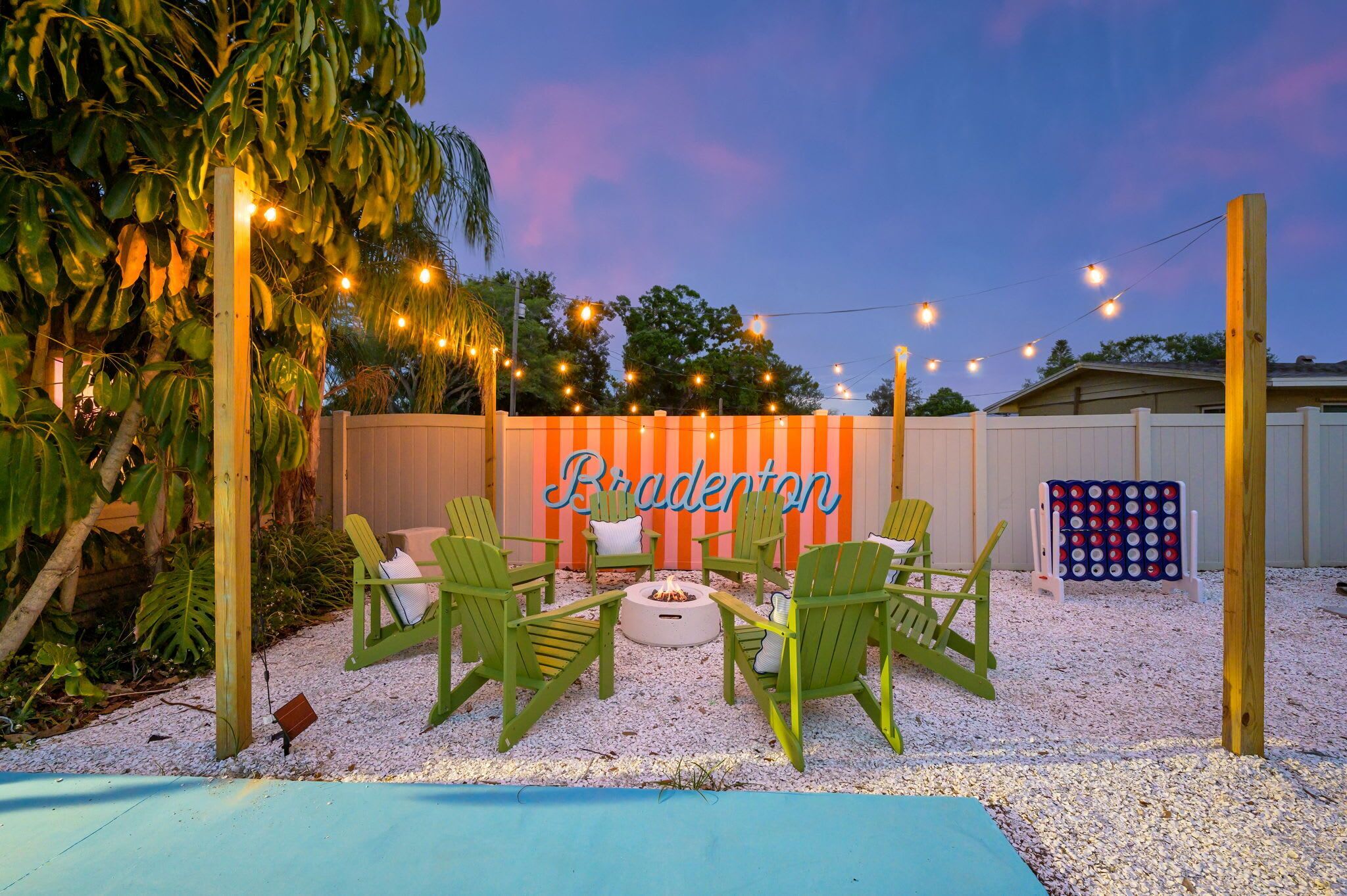 An outdoor patio with green chairs, a fire pit, string lights, and a sign reading 'Bradenton.'