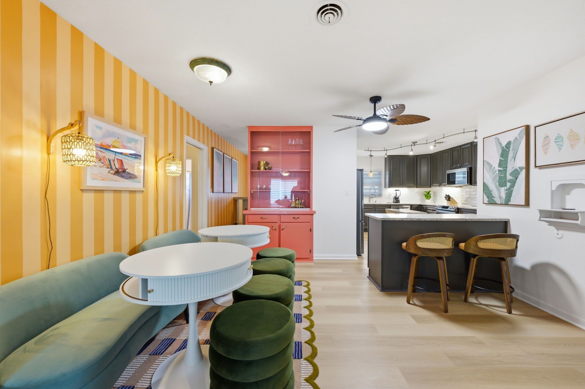 A modern living room with a sofa, ottomans, a round table, and a kitchen area with a counter and stools.