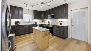A modern kitchen with dark cabinets, a central island, stainless steel appliances, and pendant lighting. - Suncourt Retreat | Sports Court | Pool | Hot Tub (Bradenton)