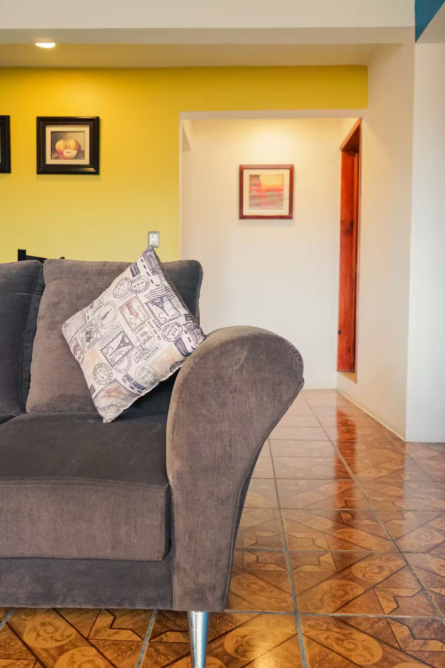 Un canapé gris avec un coussin à motifs, un mur jaune et un tableau encadré accroché au mur.