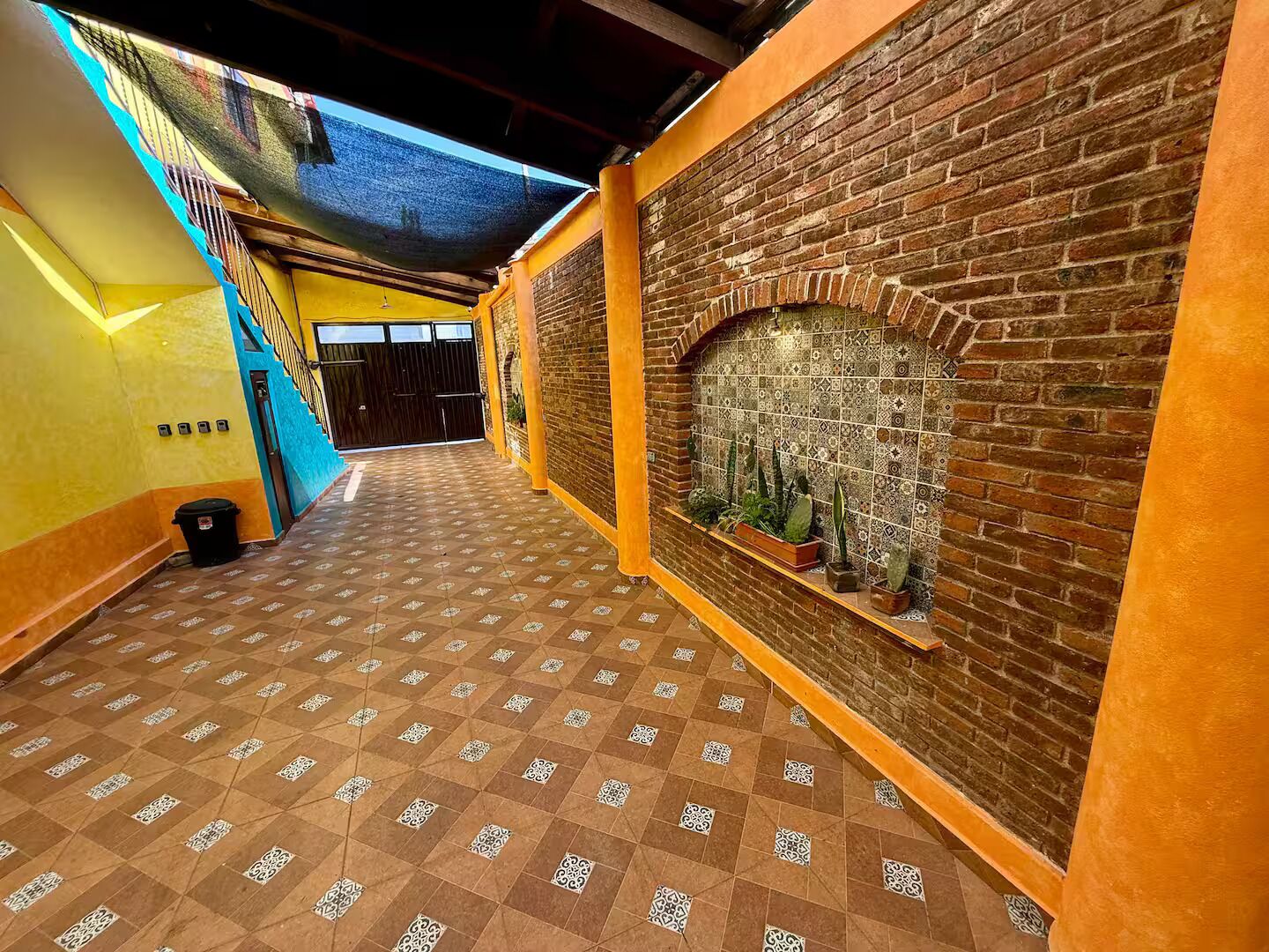A hallway with a patterned floor, a brick wall with a decorative tile section, and a staircase with a blue railing.
