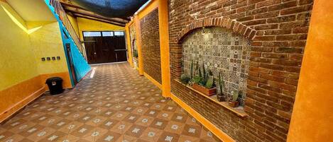 A hallway with a patterned floor, a brick wall with a decorative tile section, and a staircase with a blue railing.